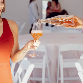 Person pouring a drink from a bottle labeled TOST into a glass, with a blurred indoor setting.
