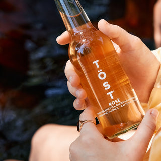 Person holding a bottle of Töst Rosé with a blurred background

