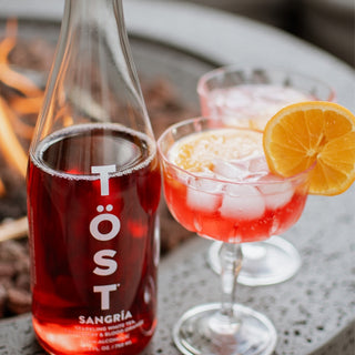 Bottle of Töst Sangria with two glasses filled with the drink on a table.
