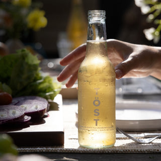 Bottle of Töst sparkling white tea on a table with a blurred background
